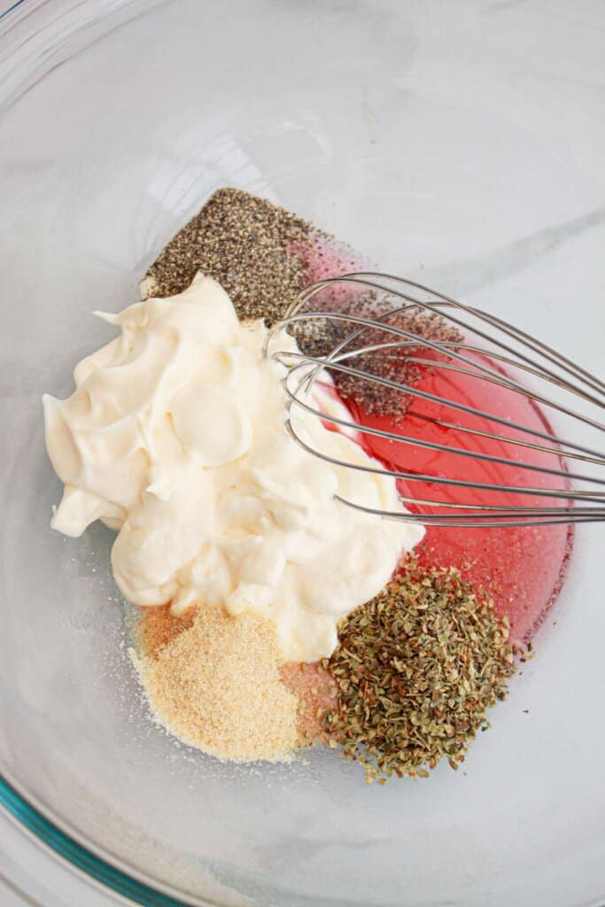 dressing being mixed with a whisk in a large glass bowl.