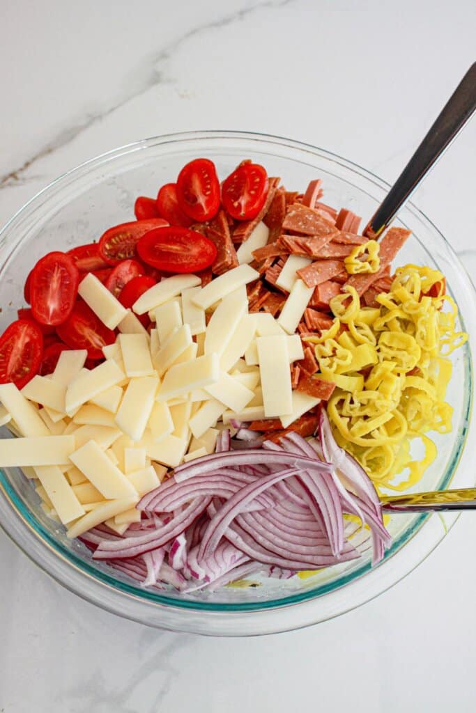 fresh vegetables, meats and cheeses being added to a large bowl.