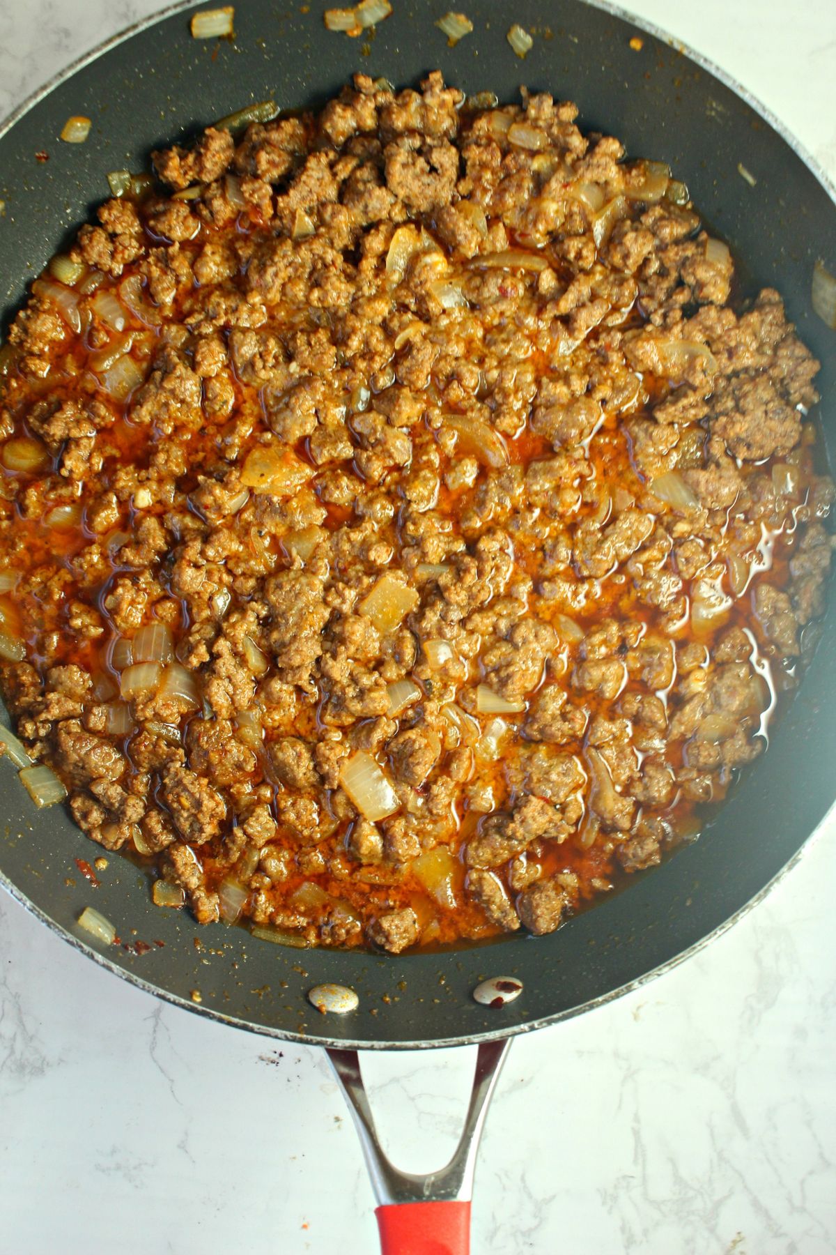 ground beef and onions being added to a skillet.