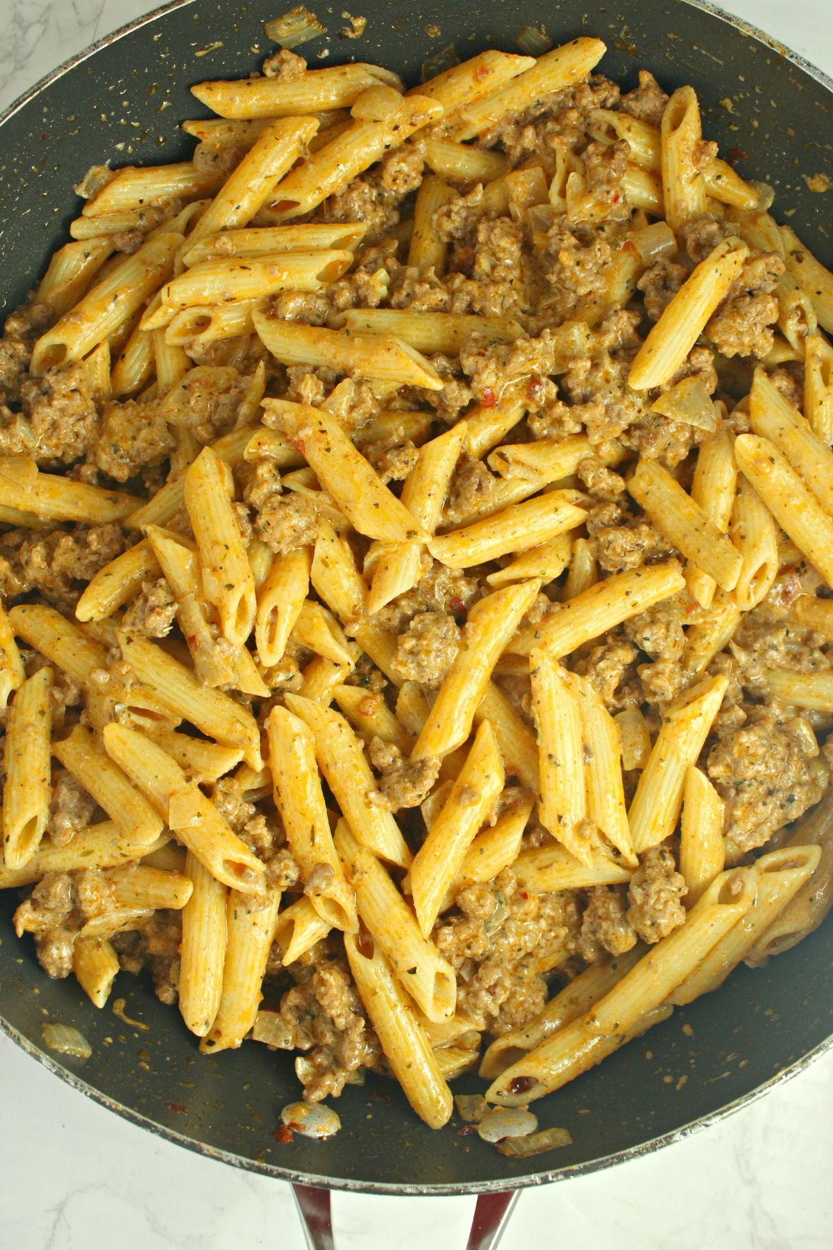 pasta and ground beef being mixed in a large skillet.