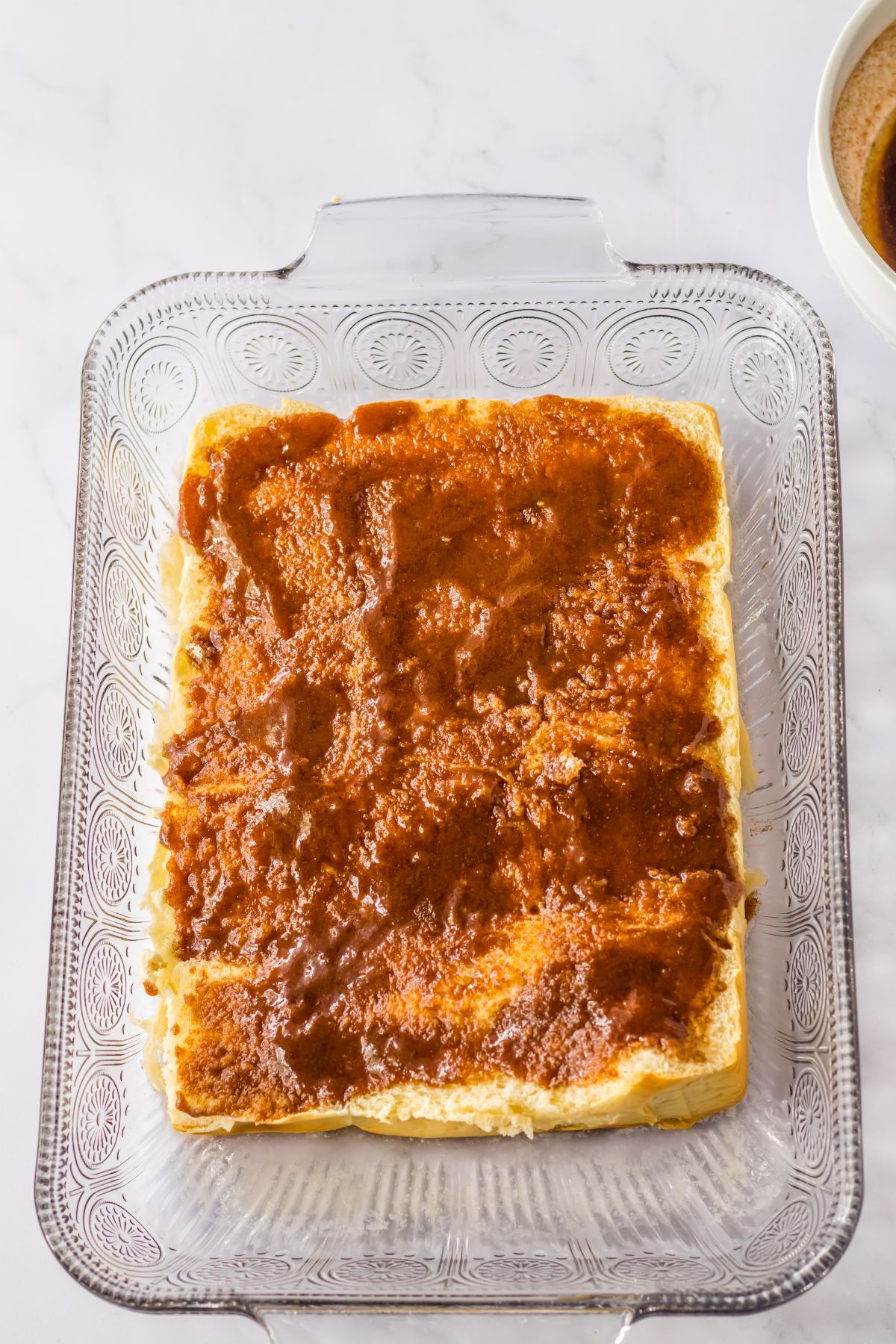 cinnamon sugar butter being spread on top of rolls in a baking dish.