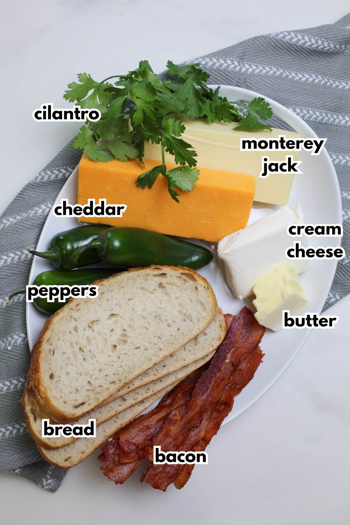 bread, peppers, cheddar cheese, monterey jack cheese, cilantro, cream cheese, butter, and baocn on a plate.