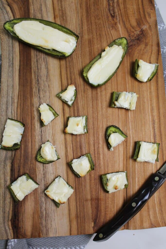cream cheese peppers being cut into pieces on a wooden cutting board.