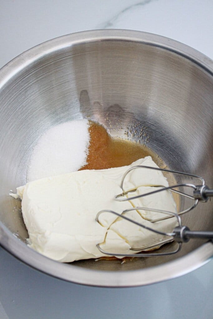 cream cheese and sugar being mixed in a stainless steel mixing bowl.