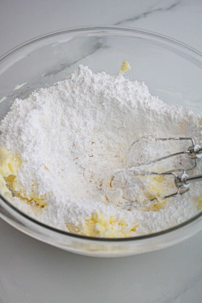 frosting being mixed in a glass mixing bowl with a hand mixer.