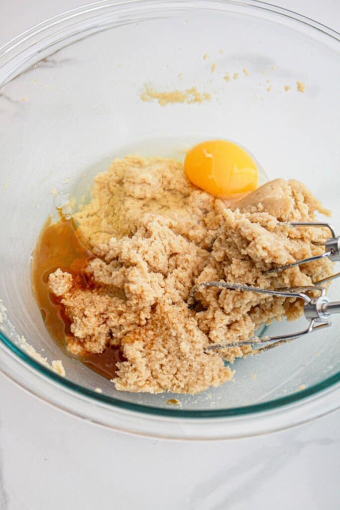 butter, sugar, egg, and vanilla extract being mixed in a glass bowl.