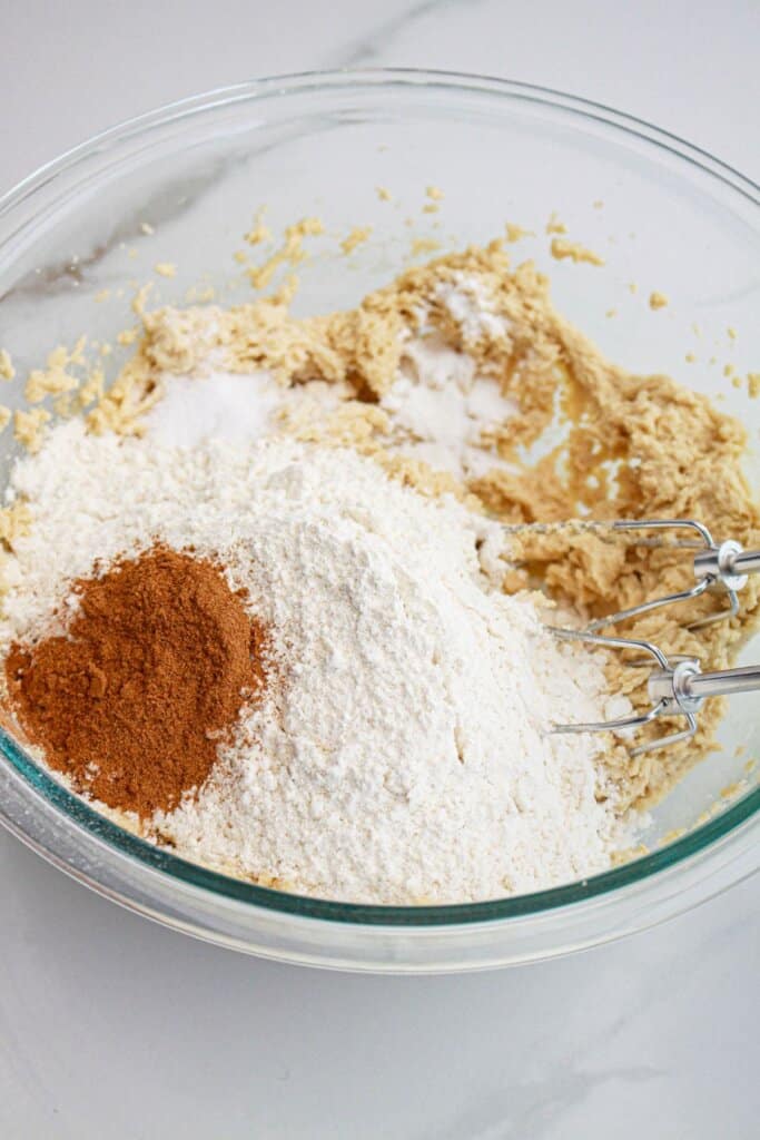 flour, cinnamon, salt and baking powder being added to dough in a glass mixing bowl.
