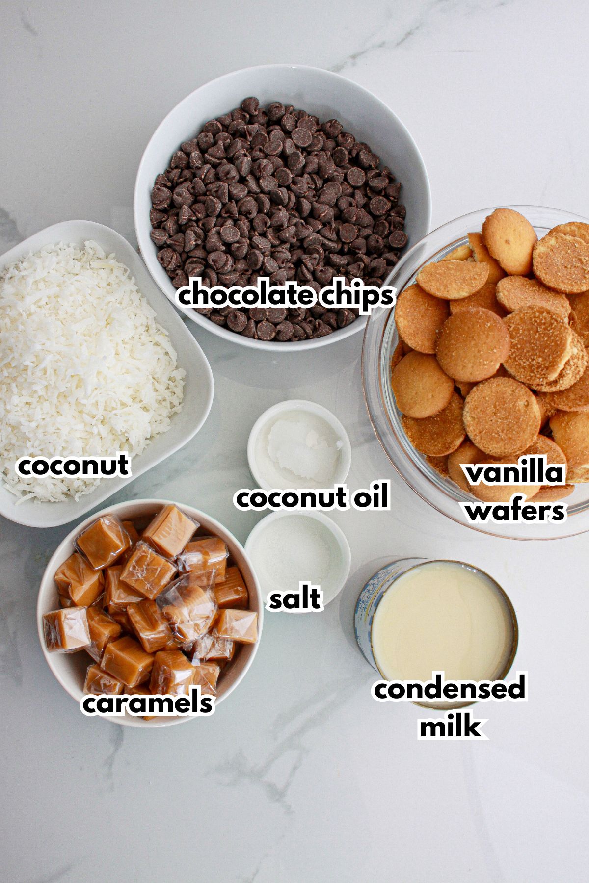 bowls of chooclate chips, coconut, vanilla wafers, caramels, coconut oil, salt, and condensed milk on a counter.