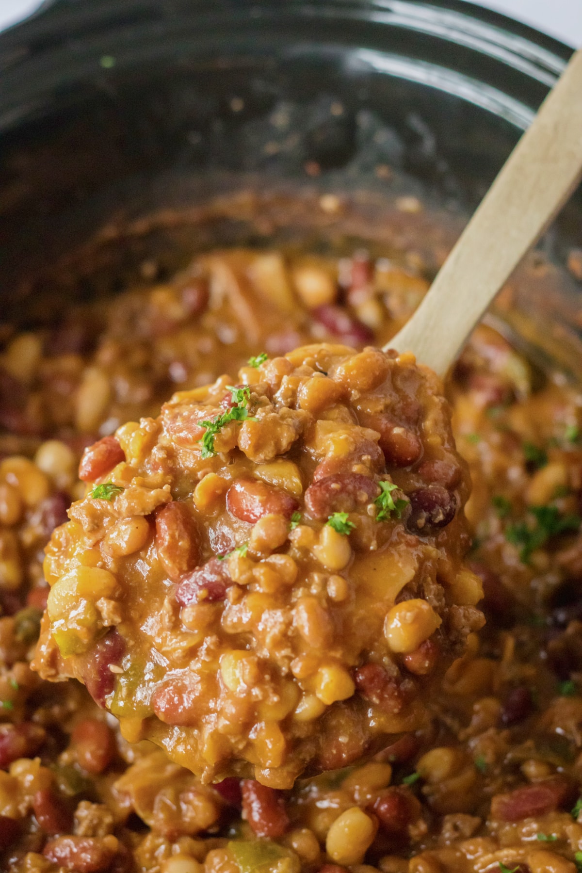 wooden spoon full of cowboy beans held above the slow cooker.