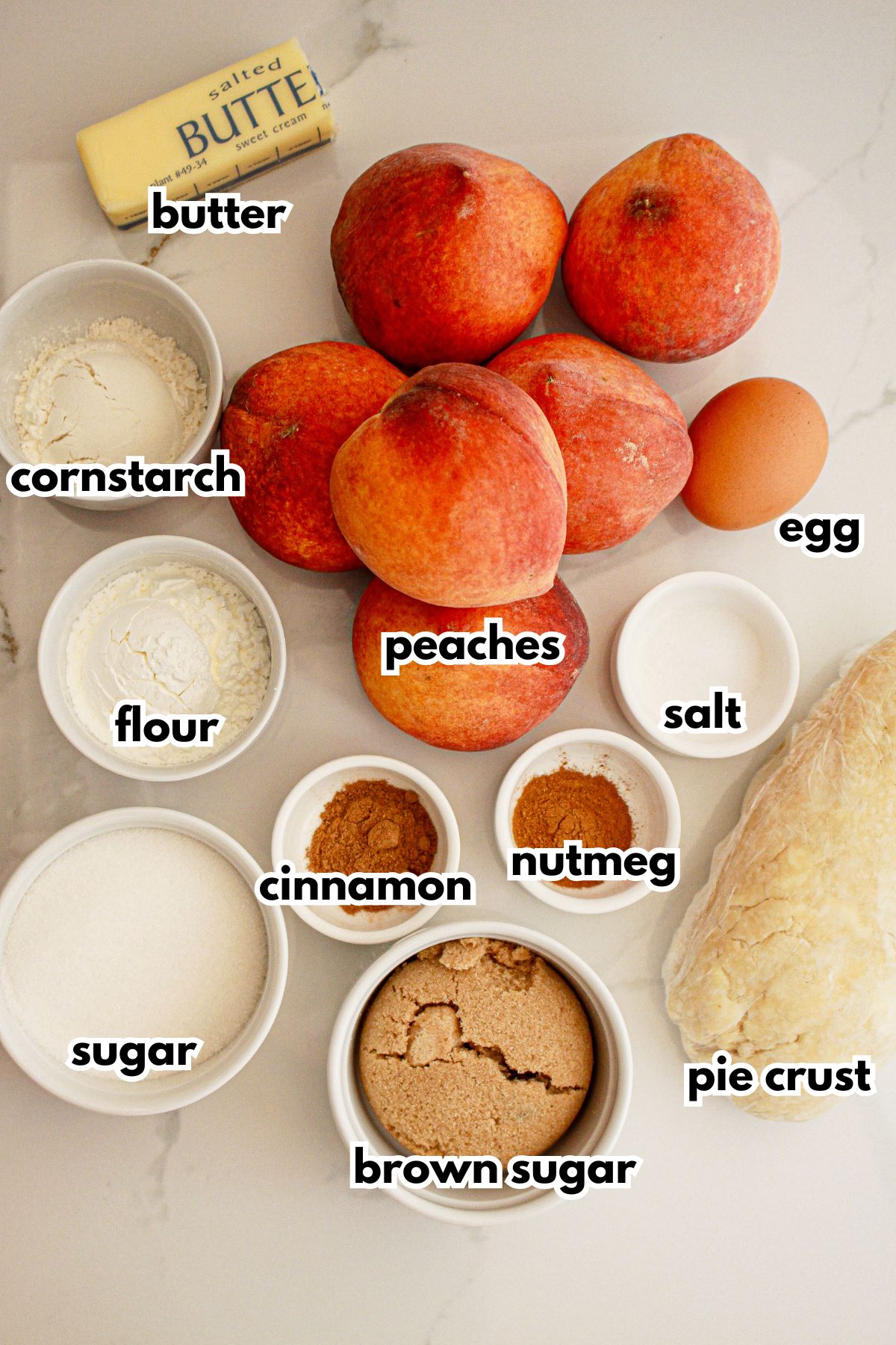 butter, peaches, cornstarch, flour, sugar, brown sugar, cinnamon, nutmeg, egg, salt, and pie crust on a counter.