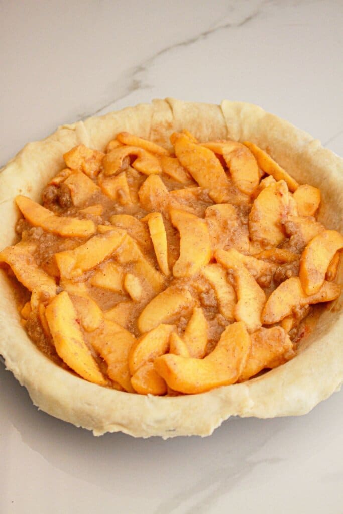 peach pie filling being added to the pie crust.