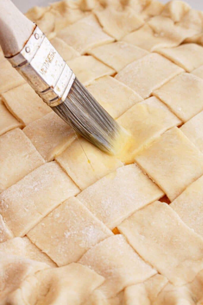 egg wash being brushed on top of the pie.