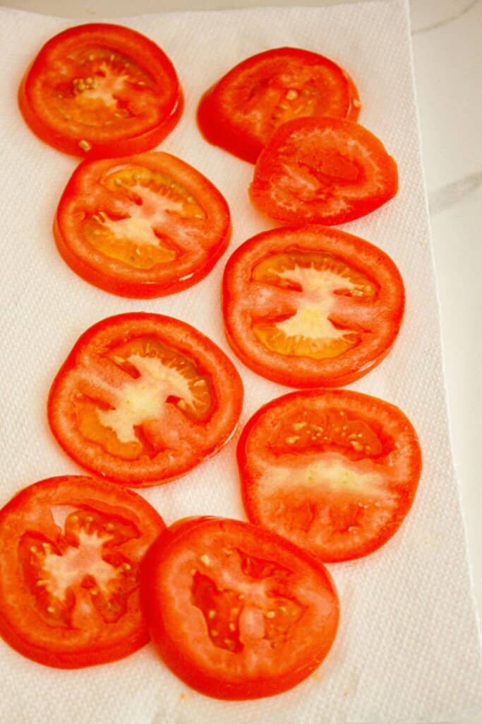 sliced tomatoes being dried on paper towels.