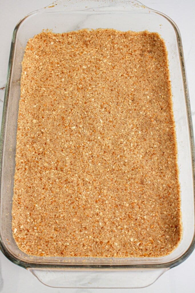 pretzel crust being pressed into a glass baking dish.