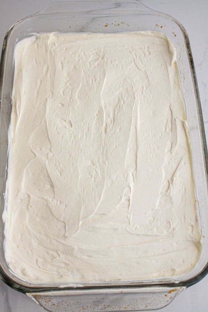 cream cheese layer being spread on top of the crust pressed into the glass baking dish.