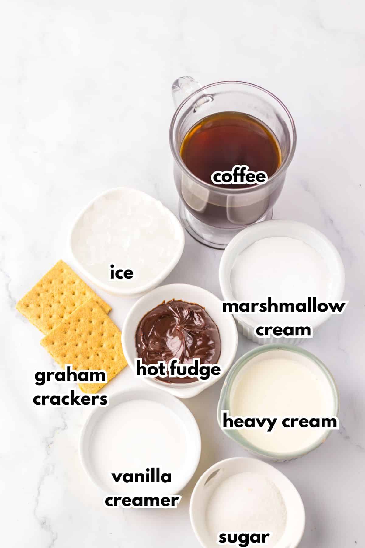 bowls of coffee, ice, graham crackers, hot fudge, marshmallow cream, vanilla creamer, sugar, and heavy cream on a counter.