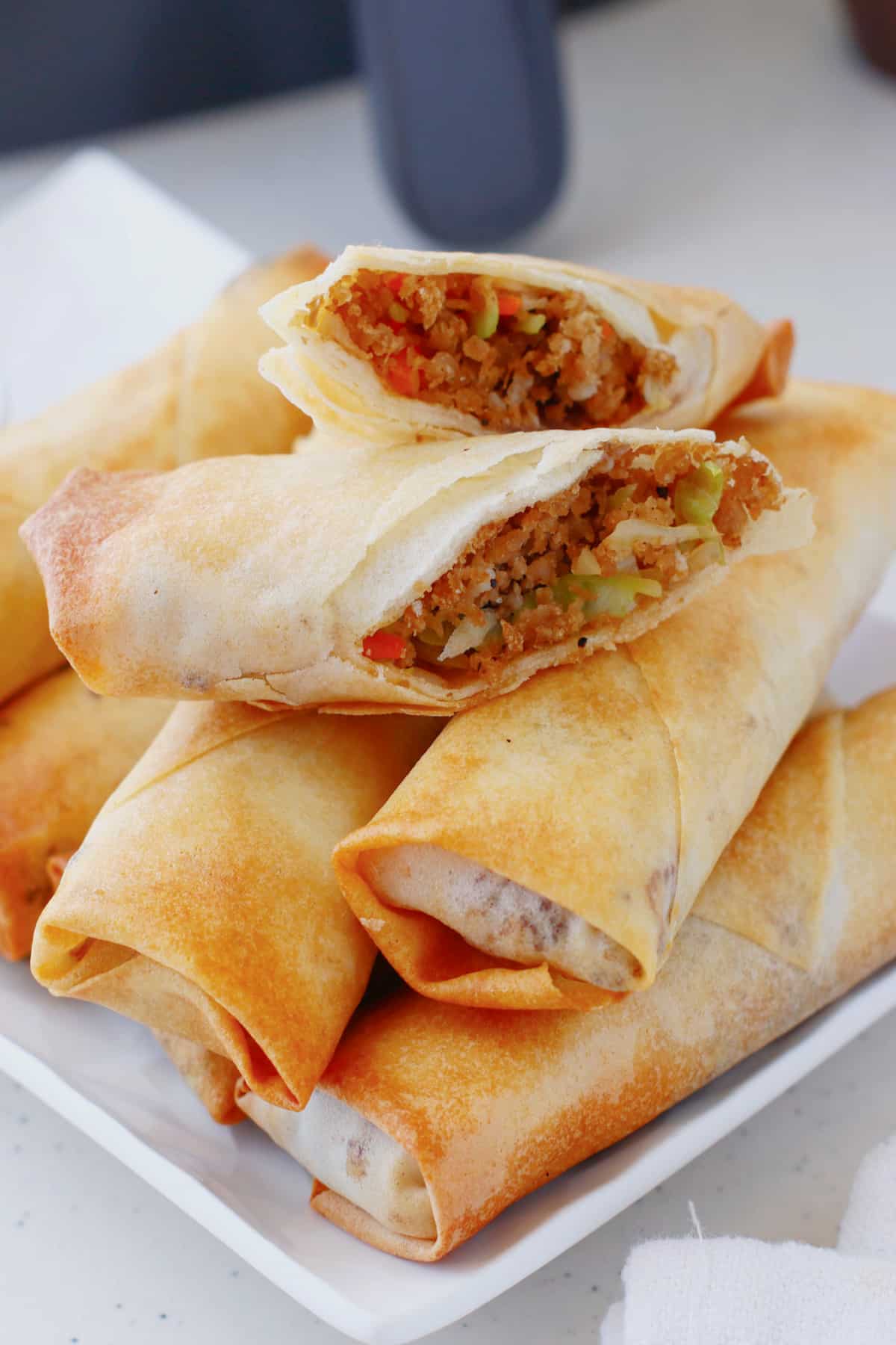 Egg rolls stacked on a serving patter with the top one broken in half.