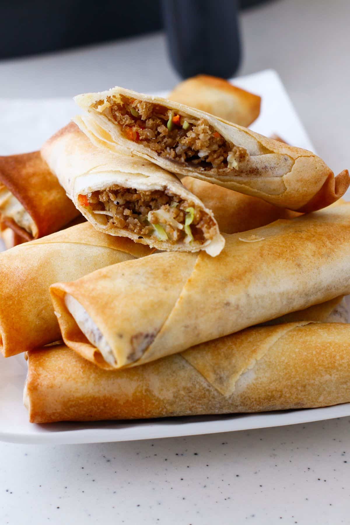 Egg rolls stacked on a serving patter with the top one broken in half.