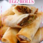 Egg rolls stacked on a serving patter with the top one broken in half.