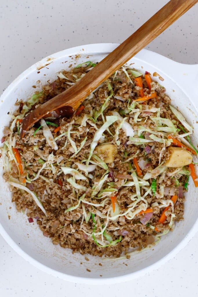 Cole slaw mix being added to a skillet with cooked ground pork.