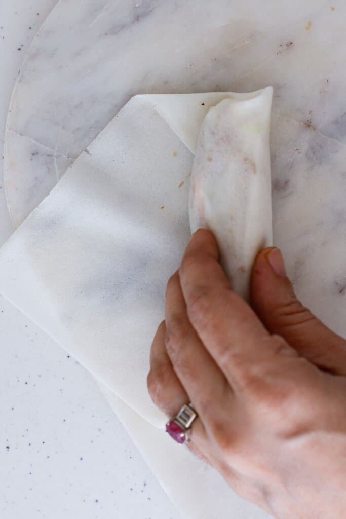 Egg roll being wrapped with a woman's hand.