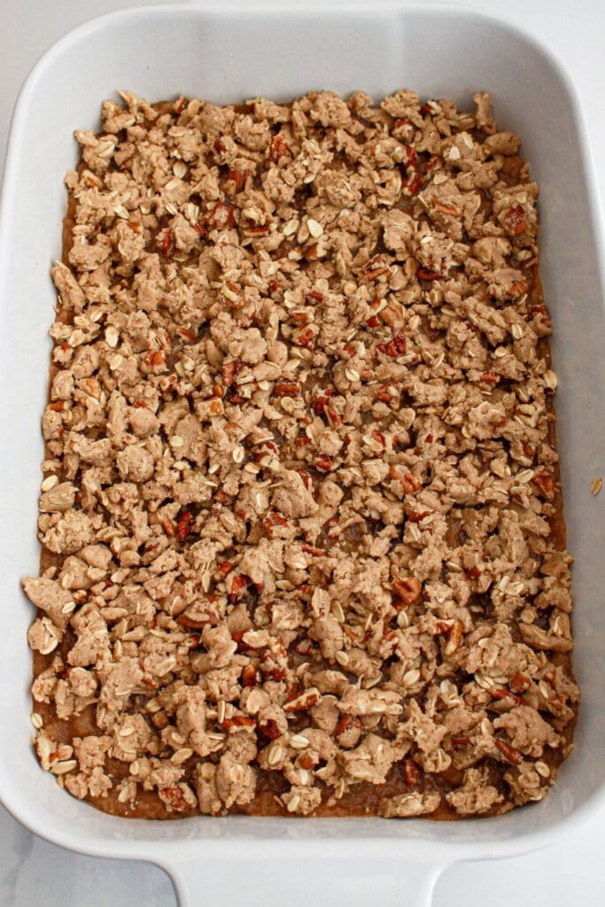 crumb topping being added to the top of a dessert in a baking dish.