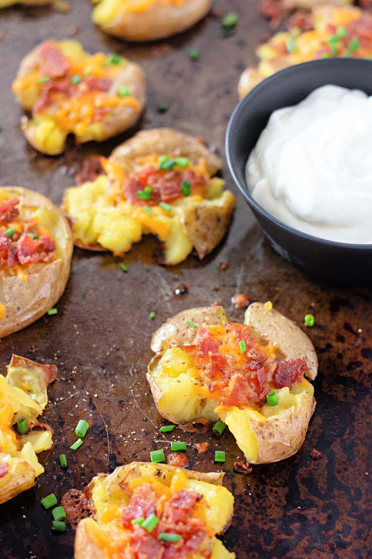 bacon cheddar smashed potaotes on a dark baking sheet.