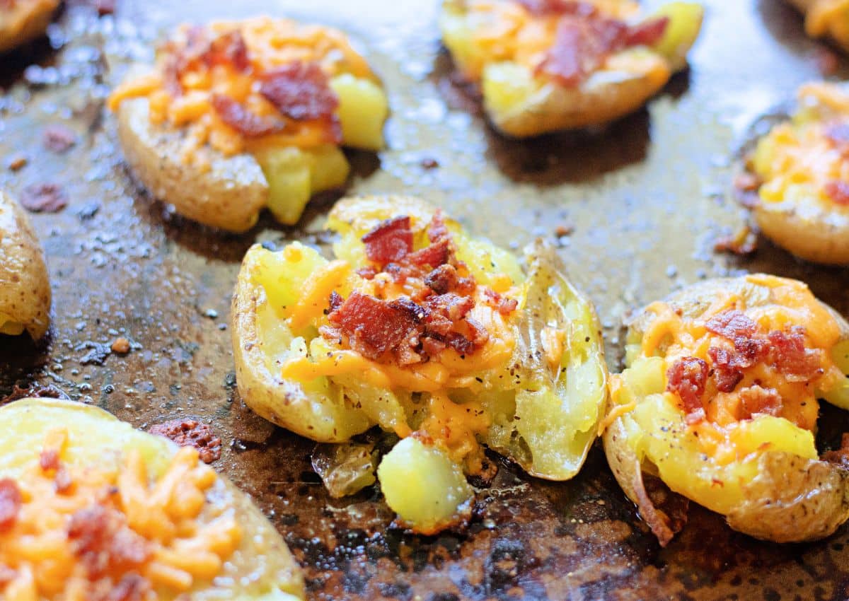 bacon cheddar smashed potaotes on a dark baking sheet.