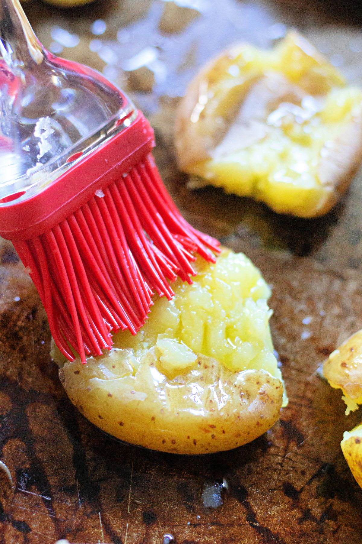 oil being brushed on top of potatoes on a baking sheet.