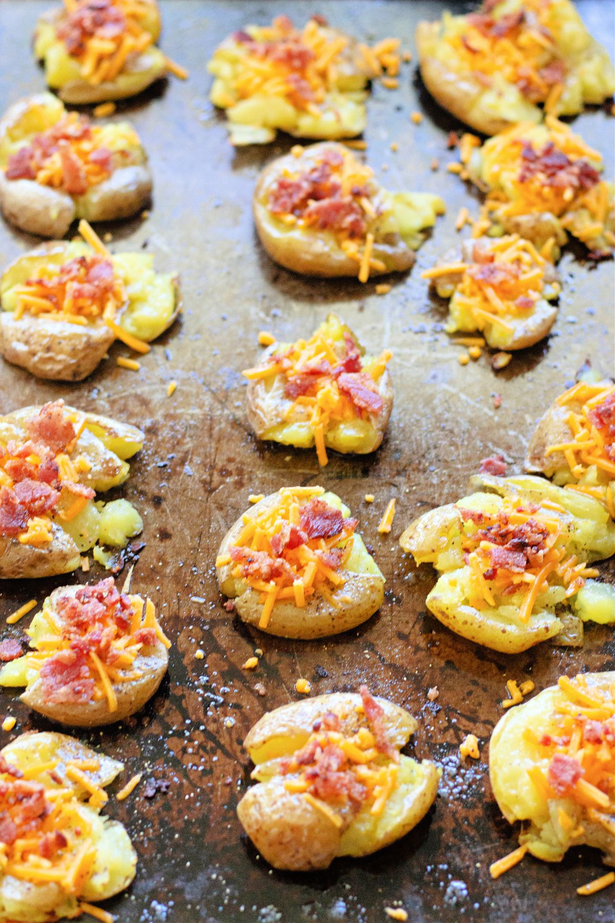 bacon cheddar smashed potaotes on a dark baking sheet.