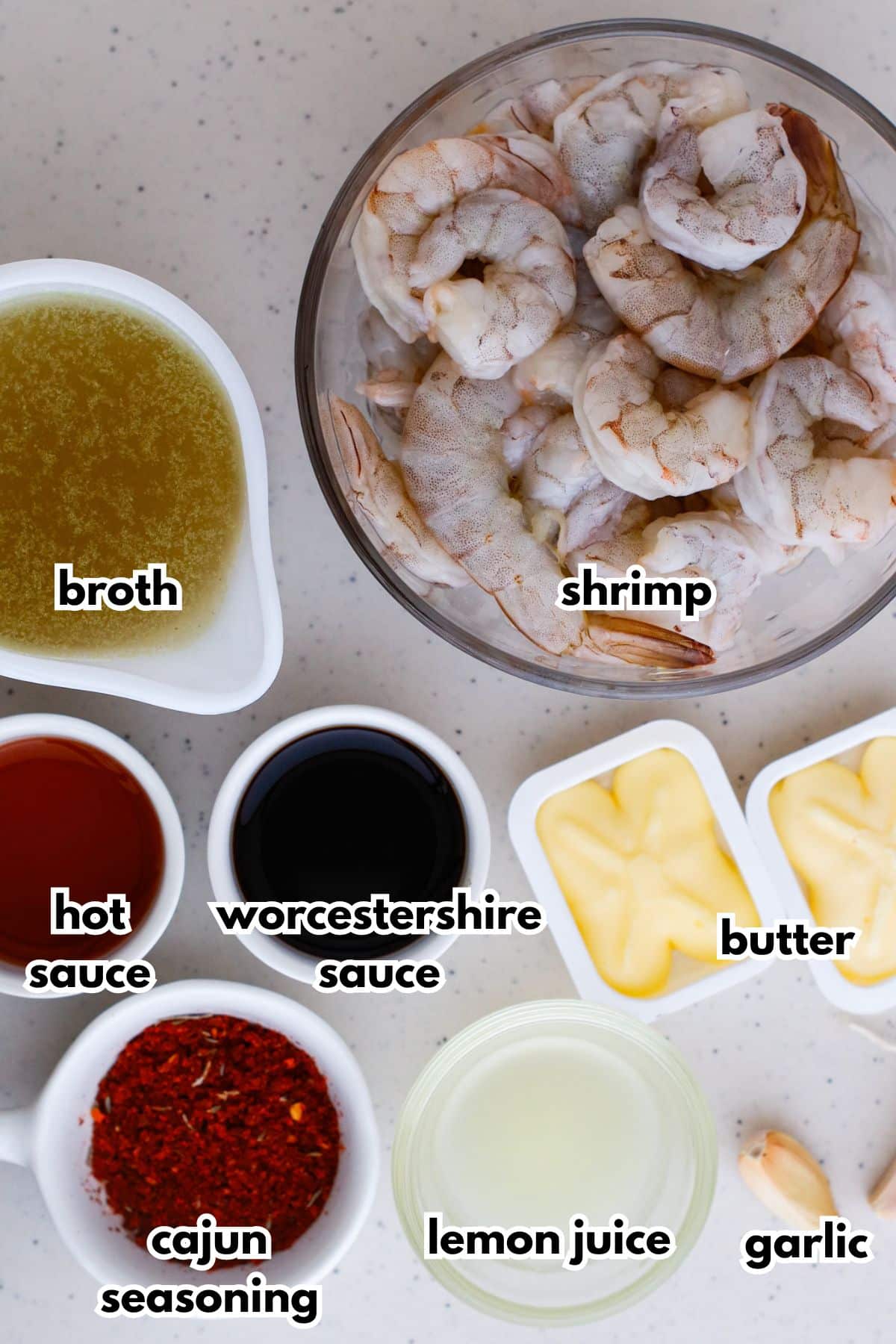 bowls of broth, shrimp, hot suace, worcestershire sauce, butter, cajun seasoning, lemon juice and garlic on a counter.