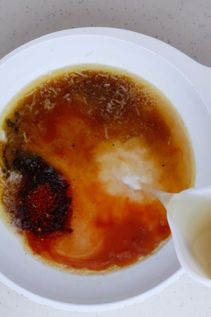 Chicken broth being added to a skillet.
