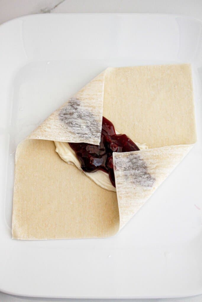Cream cheese, and pie filling being wrapped together with dough.