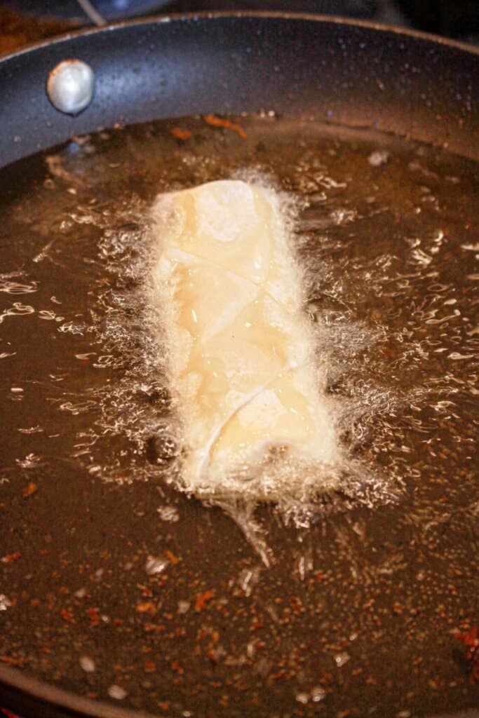 Egg roll being fried in a skillet full of oil.