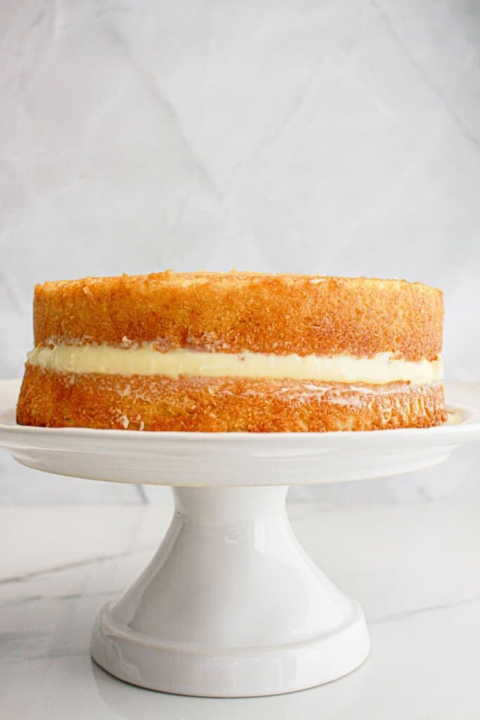 Custard being spread between two cake layers on a cake stand.