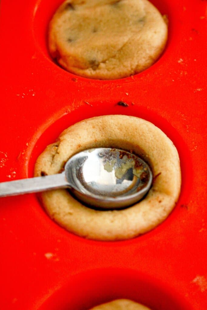 measuring spoon pressing down dough in a muffin pan.