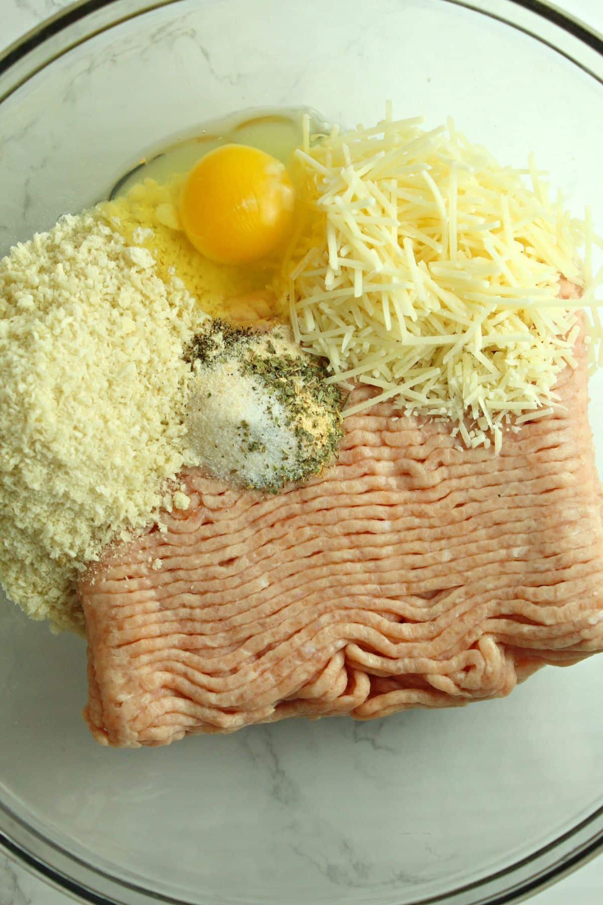 ground meat, parmesan cheese, egg, and seasonings ready to be mixed in a large bowl.