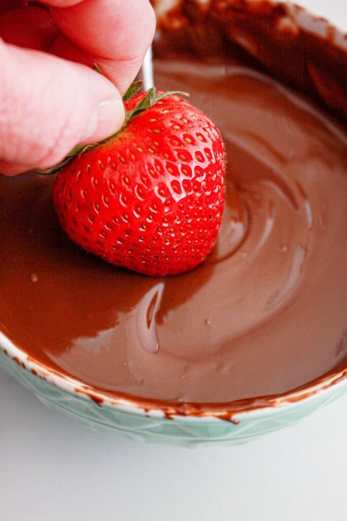 Strawberry being dipped into melted chocolate.