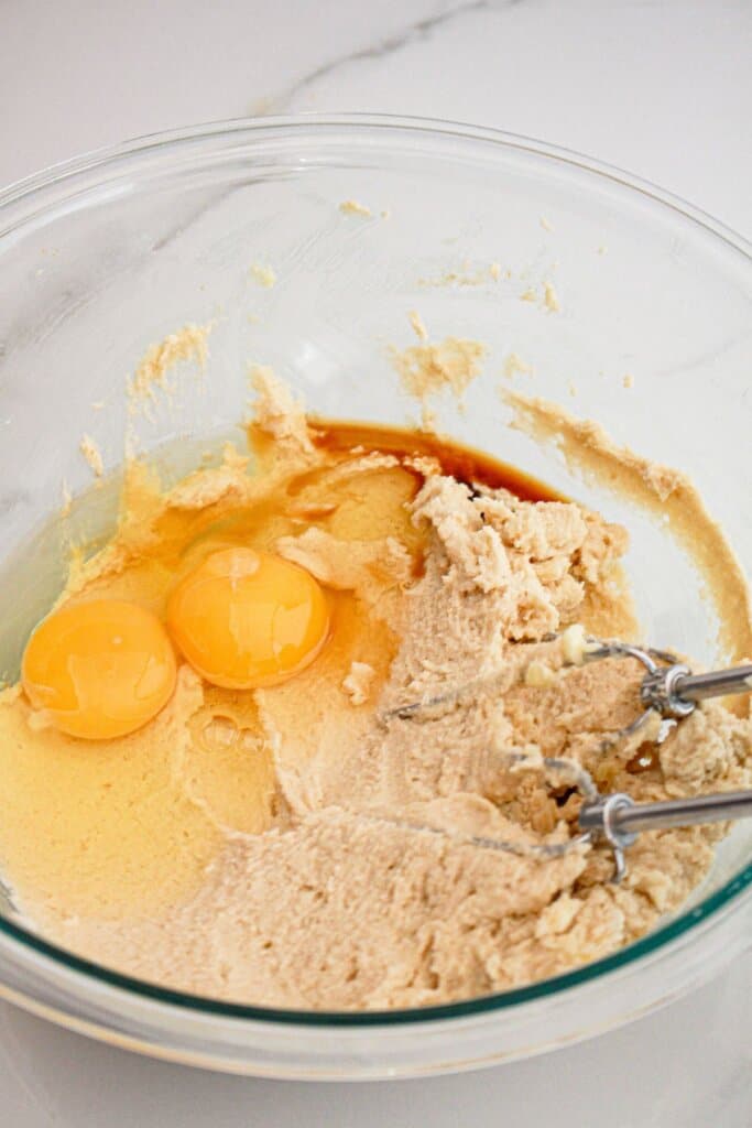 Eggs, vanilla, butter and sugar being creamed together in a glass mixng bowl with a hand mixer.
