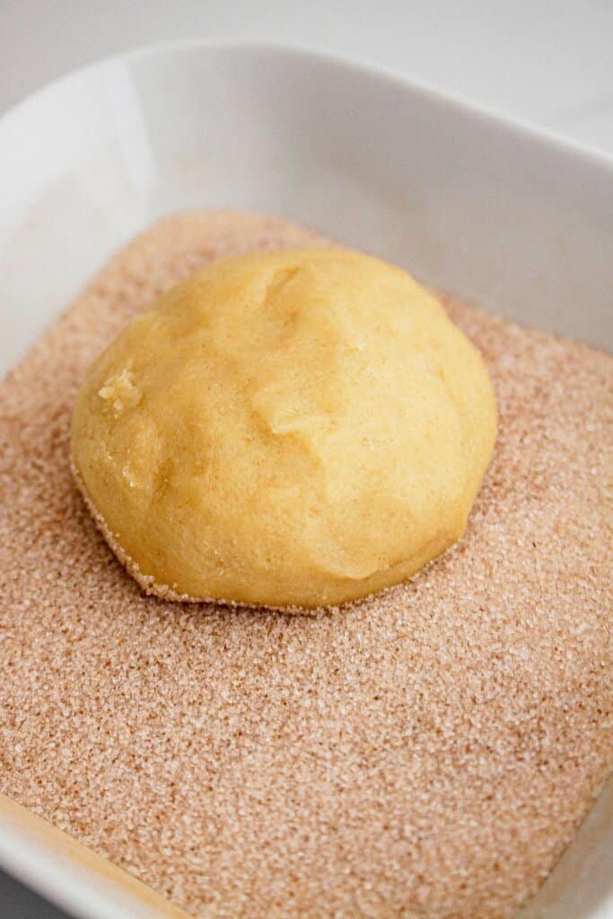 Cookie dough ball being rolled in a cinnamon sugar mixture.