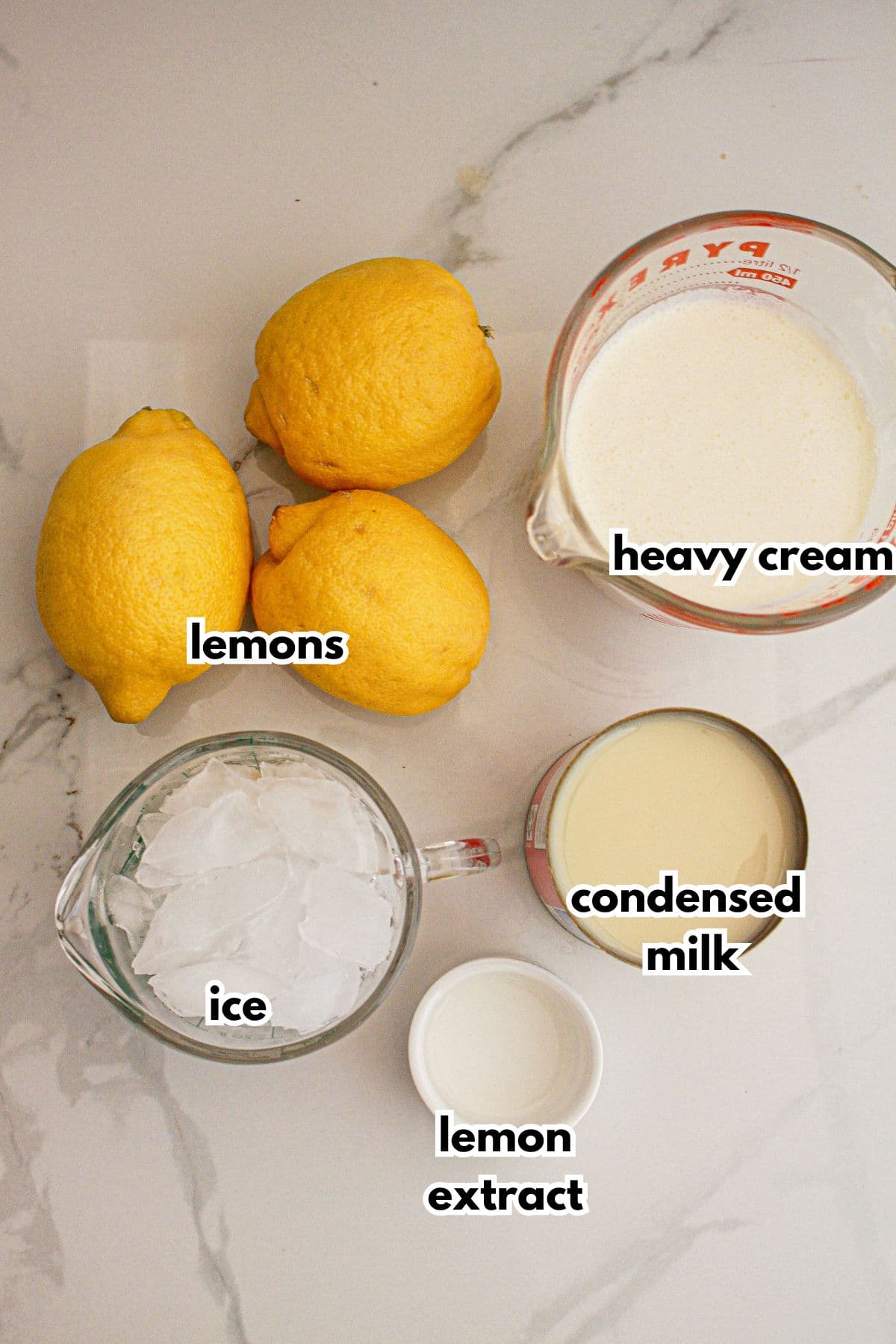 lemons, ice, lemon extract, condensed milk, and heavy cream on a counter.