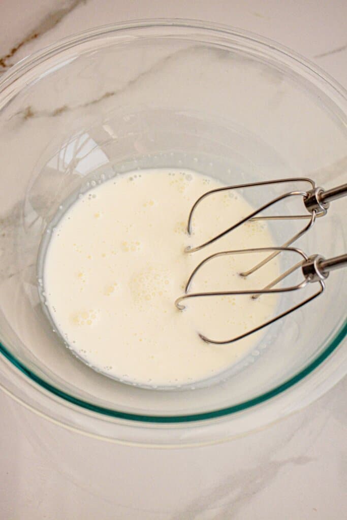 heavy cream being mixed in a glass mixing bowl with a hand mixer.