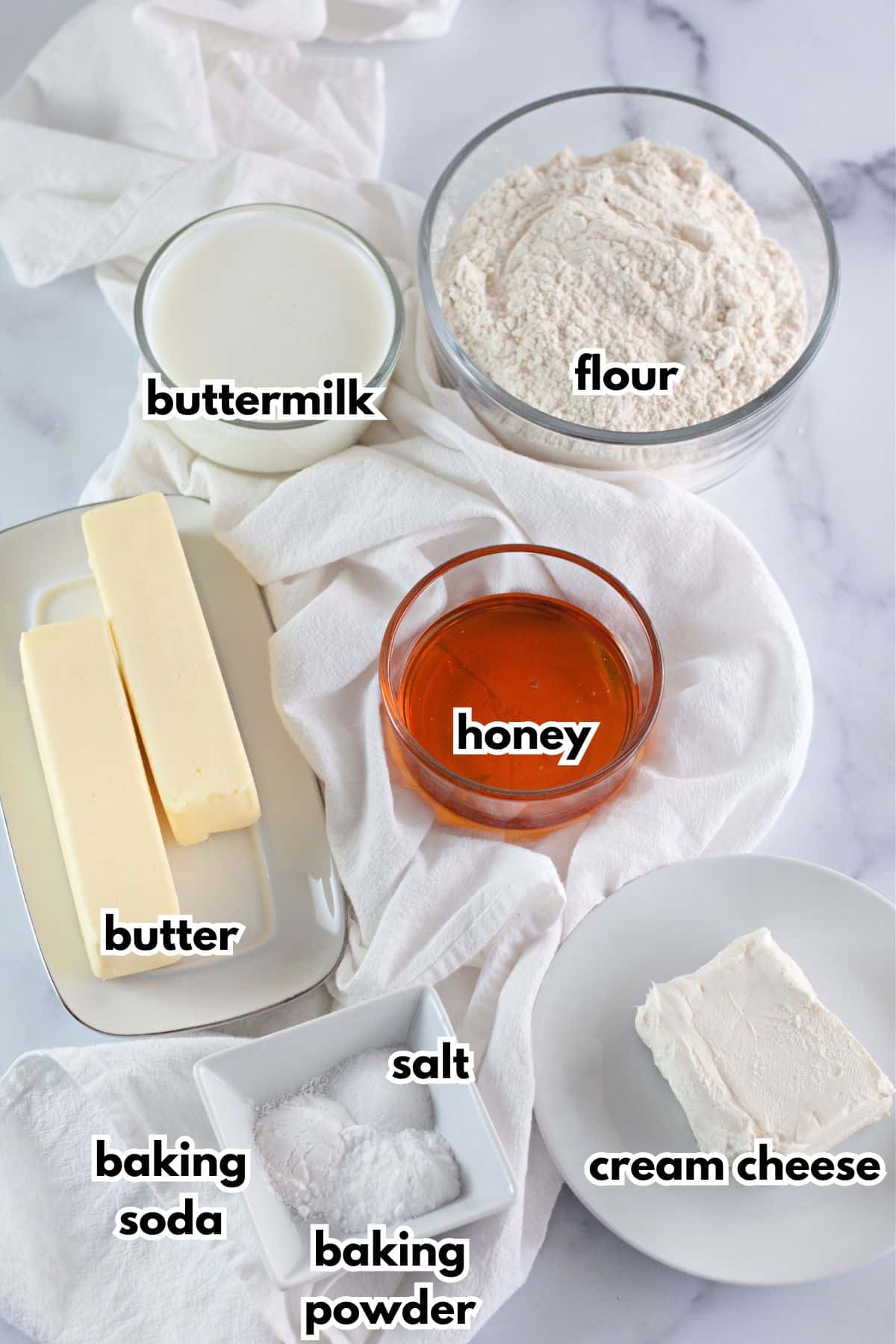 bowls of flour, buttermilk, butter, honey, baking soda, baking powder, salt and cream cheese on a counter.