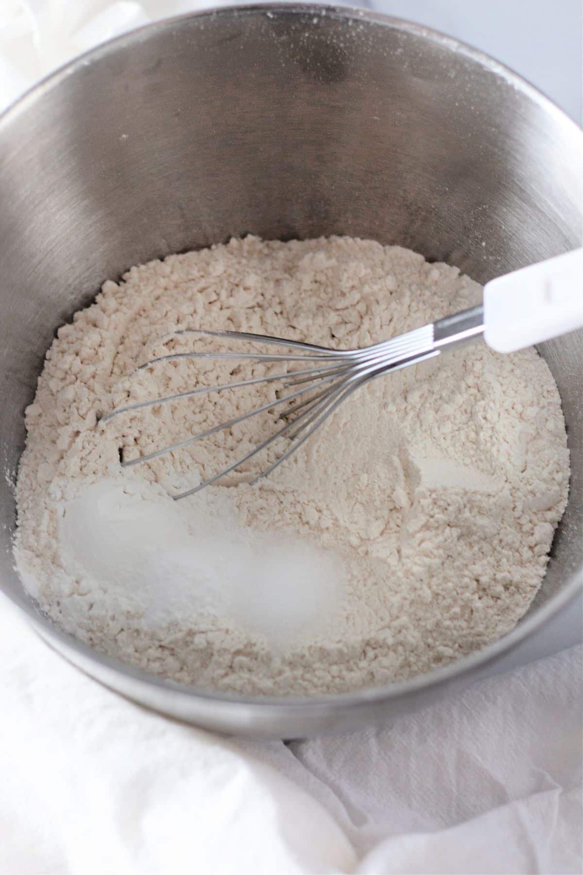 flour, baking soda, baking powder, and salt being mixed in a large bowl.