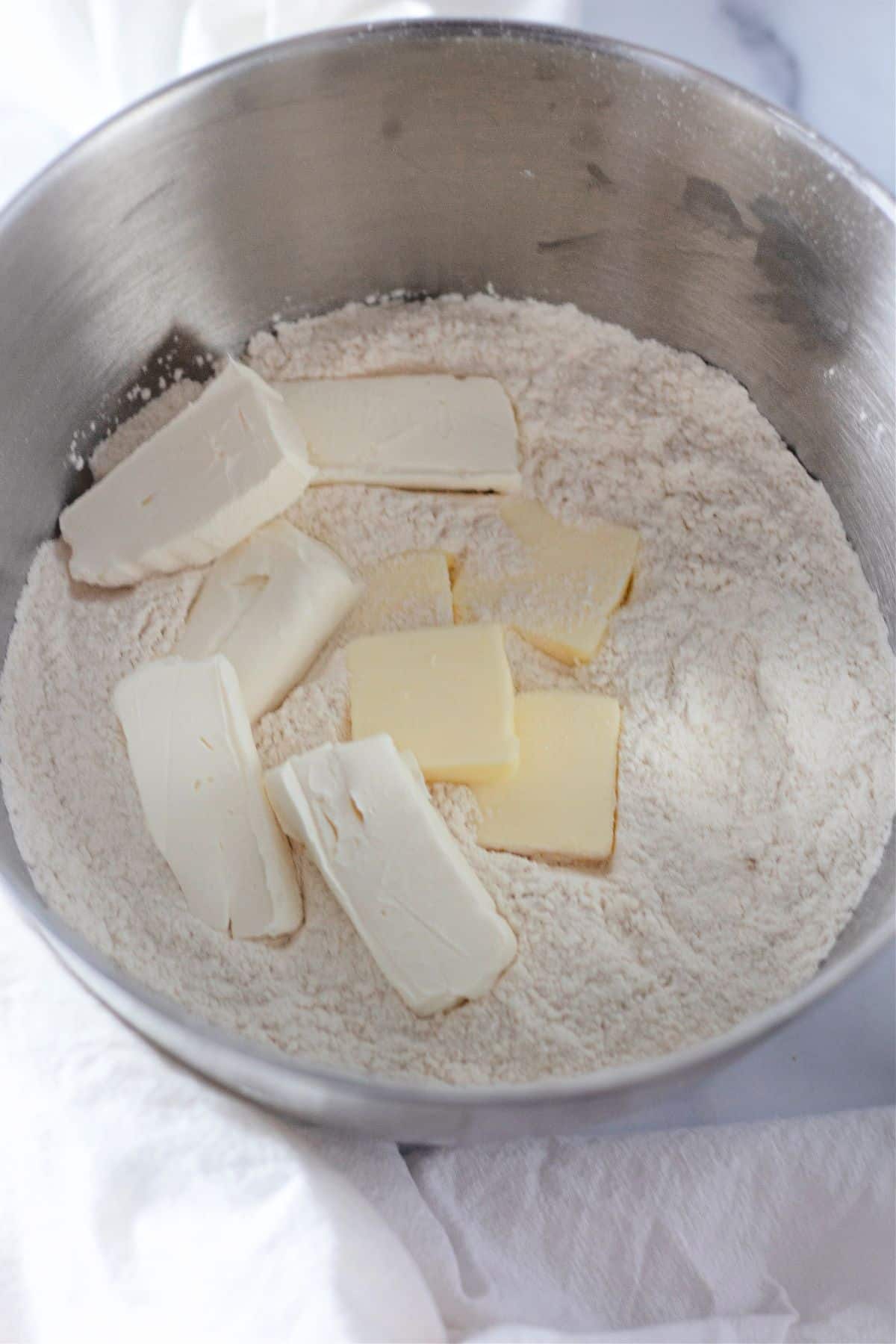 cream cheese and butter being added to flour in a stainless steel mixing bowl.