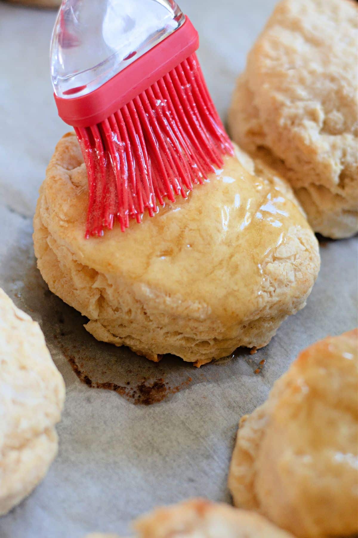 honey butter being brushed on top of the biscuits on a baking dish.