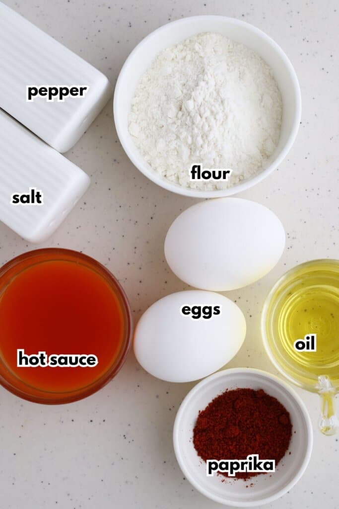 Bowls of salt, pepper, hot sauce, flour, eggs, paprika, and oil on a counter.