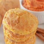 Three pumpkin buttermilk biscuits stacked on top of each other on a counter.