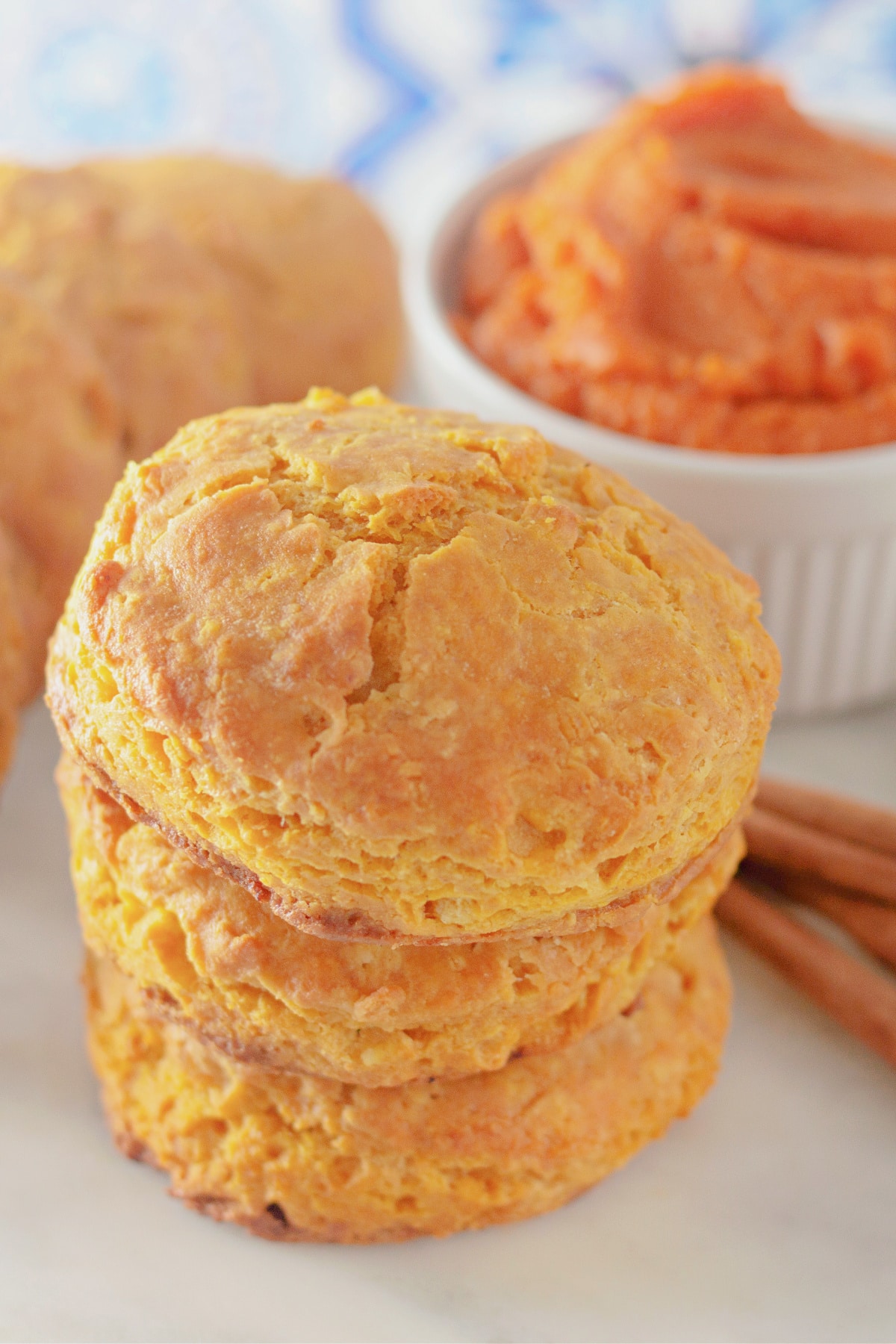 Three pumpkin buttermilk biscuits stacked on top of each other on a counter.