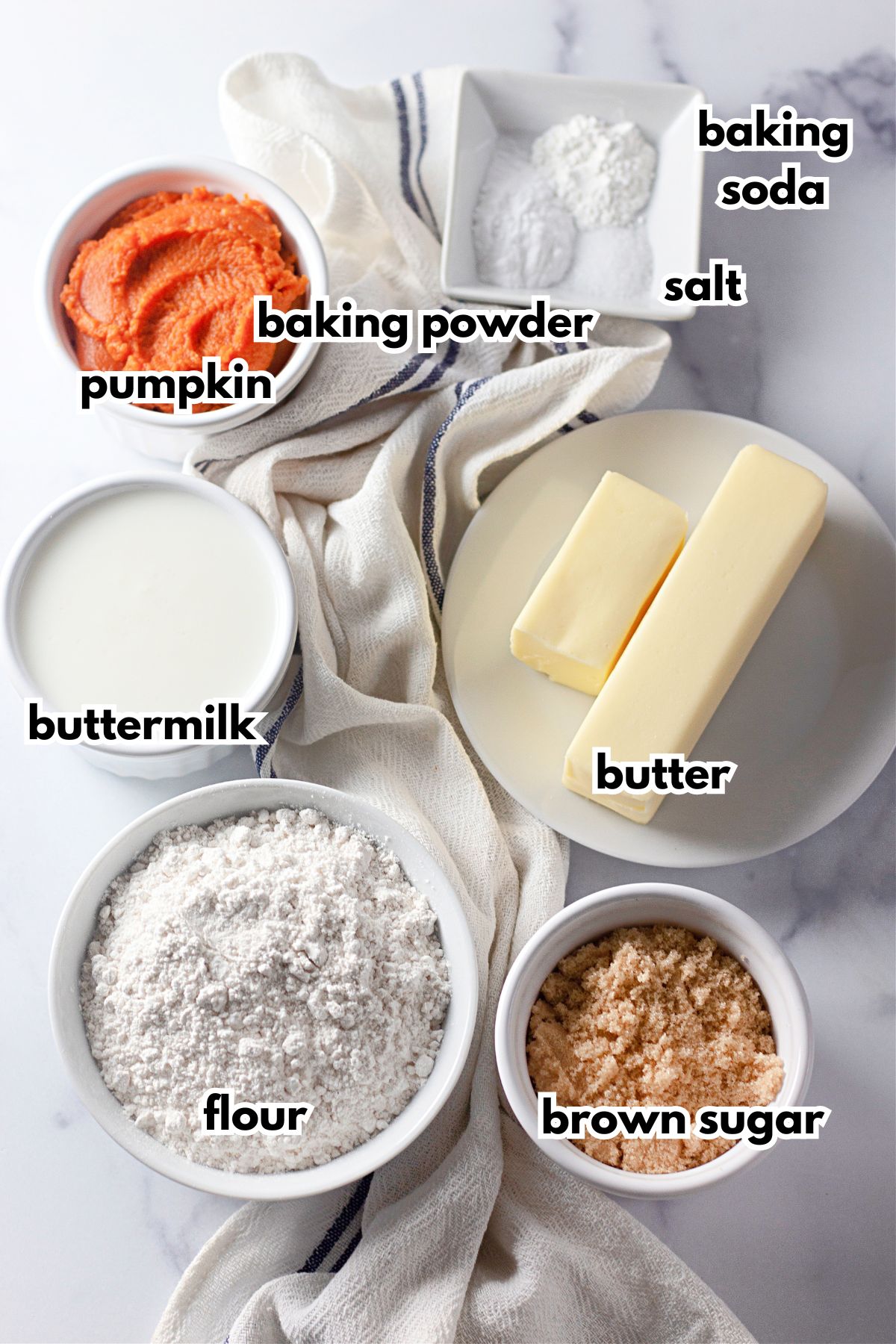 Bowls of baking soda, salt, baking powder, pumpkin, buttermilk, butter, flour, and brown sugar on a counter.